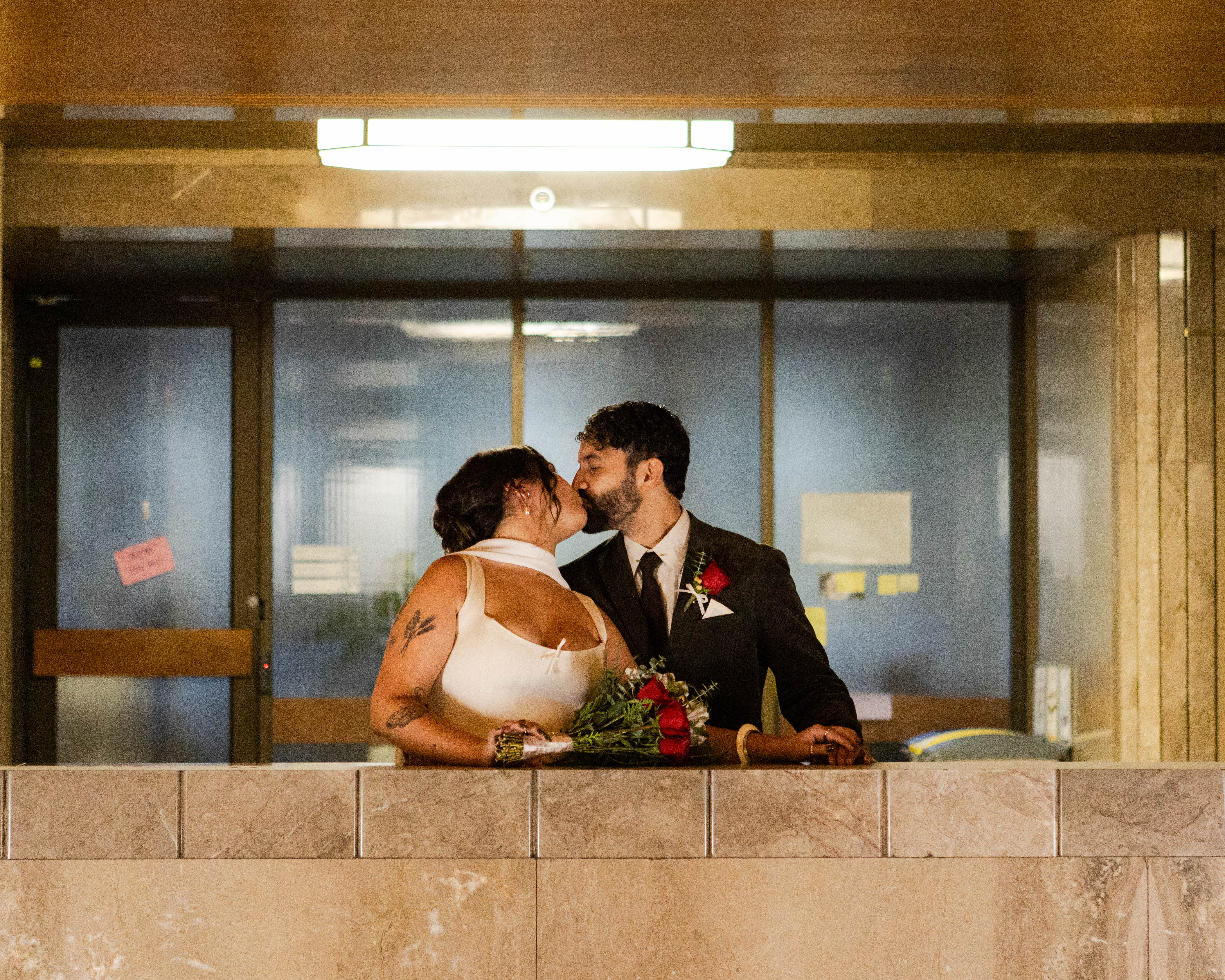 Bride and groom kissing across a tiled balcony with warm interior light behind them